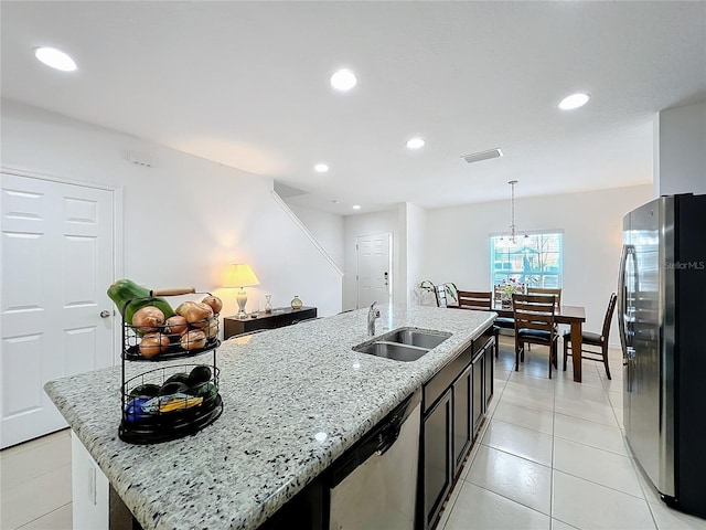 kitchen featuring sink, hanging light fixtures, stainless steel appliances, light stone countertops, and a center island with sink