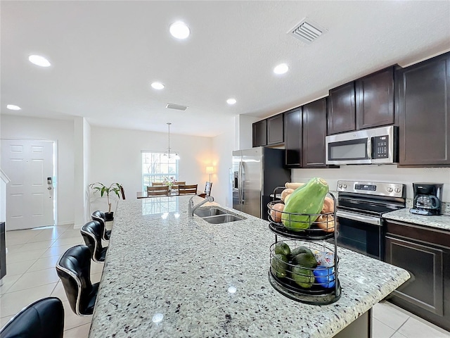 kitchen with sink, light tile patterned floors, a kitchen island with sink, stainless steel appliances, and decorative light fixtures