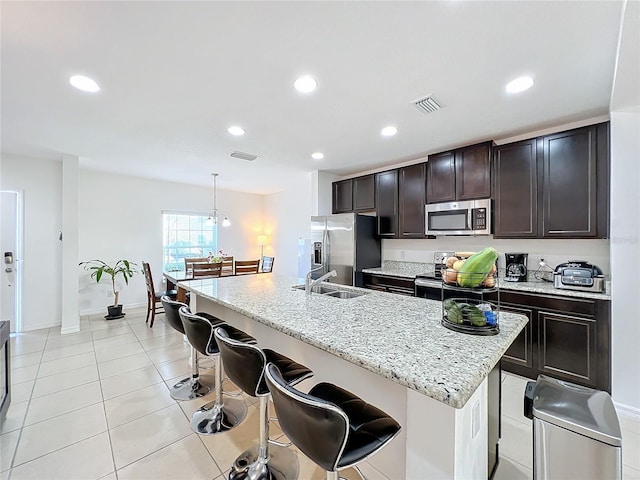 kitchen featuring an island with sink, sink, a kitchen bar, hanging light fixtures, and stainless steel appliances