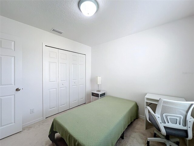 bedroom with a closet, light carpet, and a textured ceiling