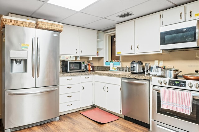 kitchen with sink, a paneled ceiling, white cabinetry, stainless steel appliances, and light hardwood / wood-style floors