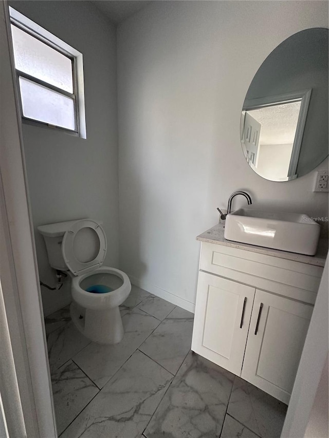 bathroom with toilet, marble finish floor, baseboards, and vanity