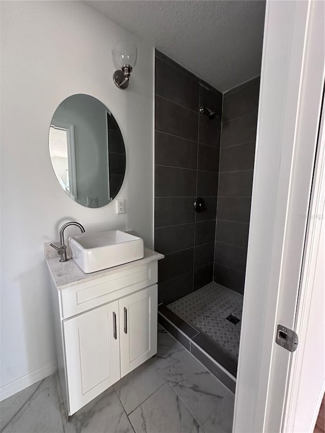 bathroom with a textured ceiling, vanity, baseboards, marble finish floor, and a tile shower