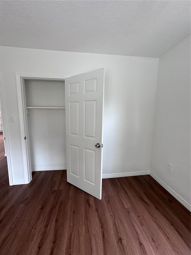 unfurnished bedroom featuring a closet, a textured ceiling, baseboards, and dark wood-style flooring