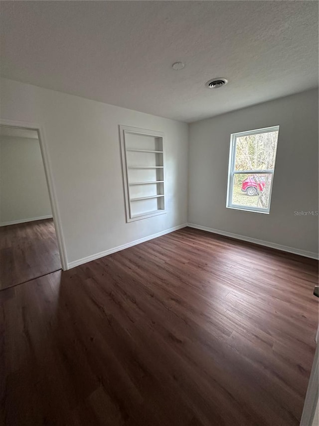 unfurnished bedroom featuring a textured ceiling, dark wood finished floors, visible vents, and baseboards