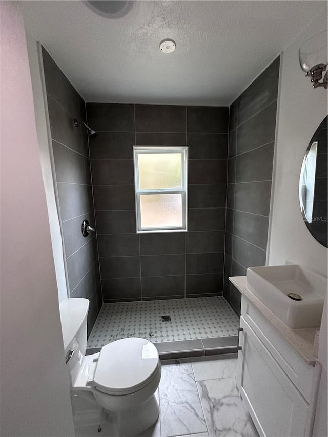 bathroom featuring a textured ceiling, toilet, vanity, marble finish floor, and a shower stall