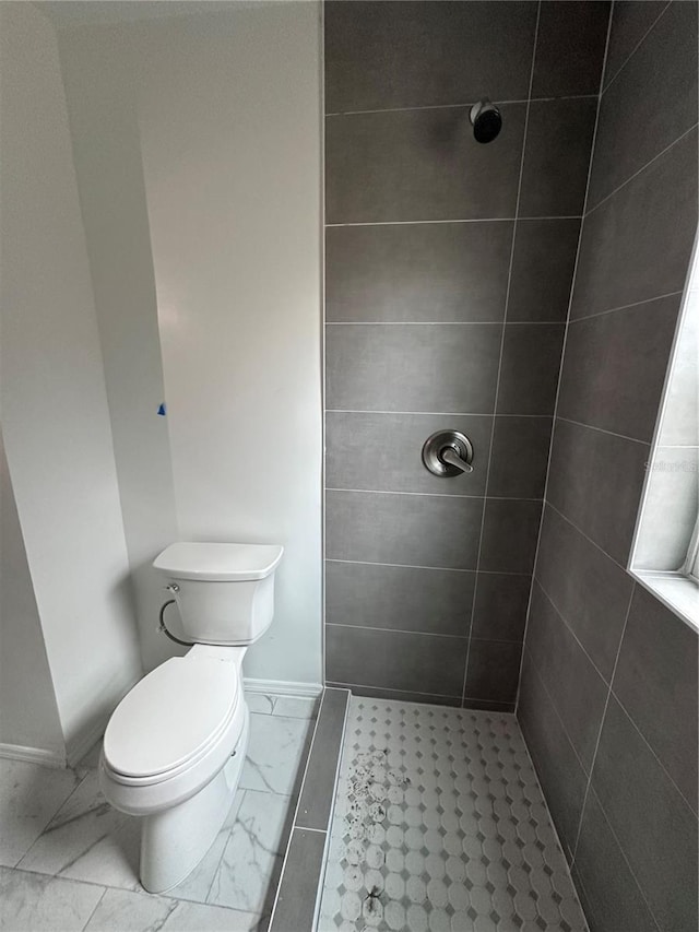 bathroom featuring toilet, marble finish floor, baseboards, and tiled shower