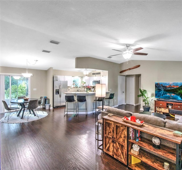 living room with dark wood-type flooring, ceiling fan, vaulted ceiling, and a textured ceiling