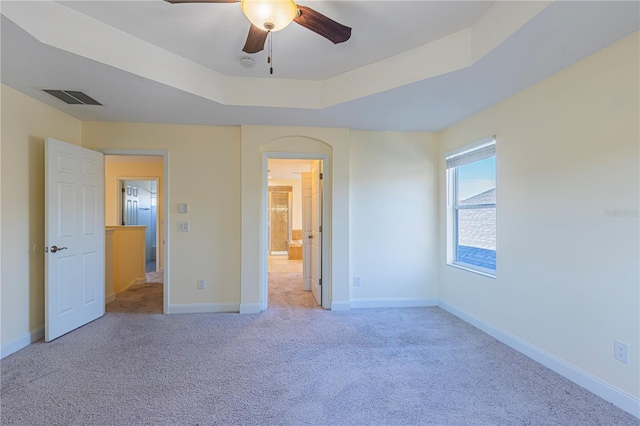 unfurnished bedroom featuring light carpet, connected bathroom, a raised ceiling, and ceiling fan