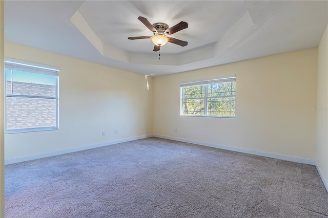 carpeted empty room featuring ceiling fan and a raised ceiling