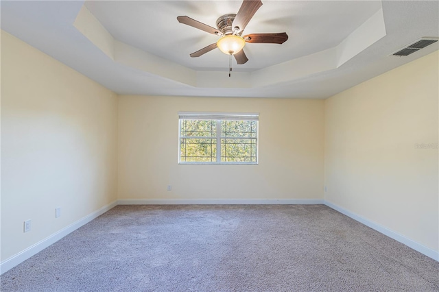 carpeted empty room with a raised ceiling and ceiling fan