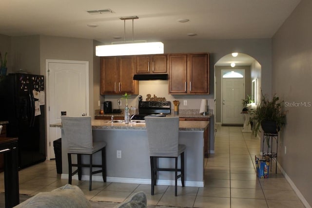 kitchen with light stone counters, hanging light fixtures, black appliances, and a kitchen bar