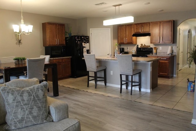 kitchen featuring an island with sink, a chandelier, a kitchen breakfast bar, hanging light fixtures, and black appliances