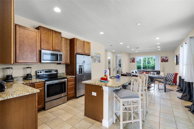 kitchen with sink, light stone countertops, an island with sink, and appliances with stainless steel finishes