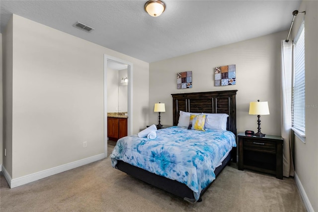 carpeted bedroom with ensuite bathroom and a textured ceiling