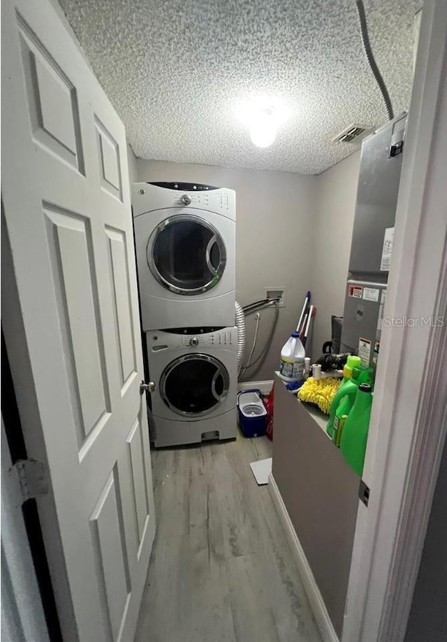 washroom featuring stacked washer and clothes dryer, light hardwood / wood-style flooring, and a textured ceiling