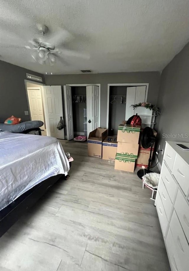 bedroom featuring ceiling fan, two closets, a textured ceiling, and light wood-type flooring