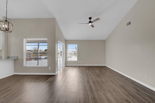 unfurnished living room with dark wood-style floors, visible vents, vaulted ceiling, baseboards, and ceiling fan with notable chandelier