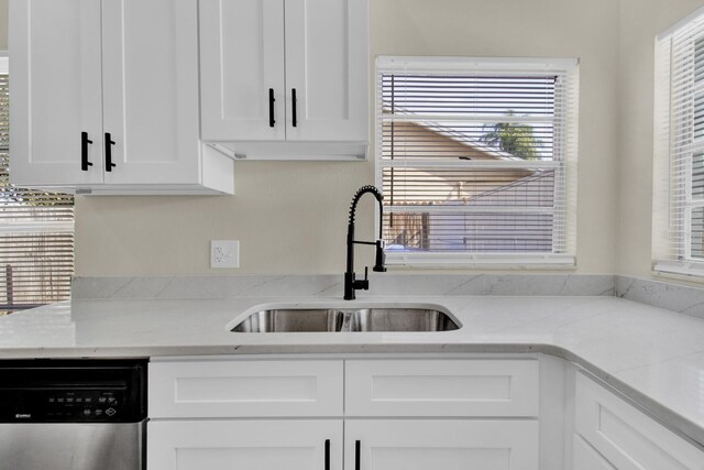 kitchen with light stone counters, white cabinets, a sink, and stainless steel dishwasher