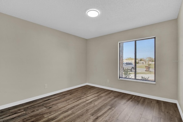 empty room with a textured ceiling, baseboards, and dark wood-type flooring