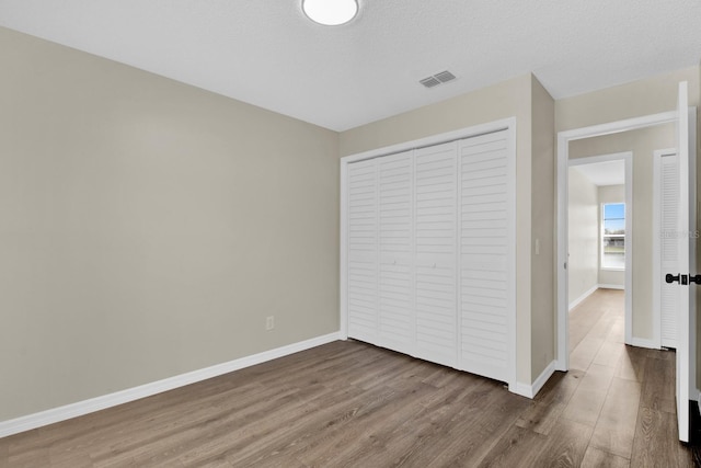 unfurnished bedroom featuring a closet, wood finished floors, visible vents, and baseboards