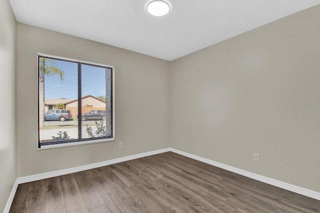 empty room featuring a textured ceiling, dark wood-style flooring, and baseboards