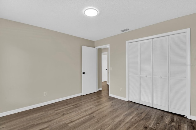 unfurnished bedroom with dark wood-style flooring, visible vents, a textured ceiling, and baseboards