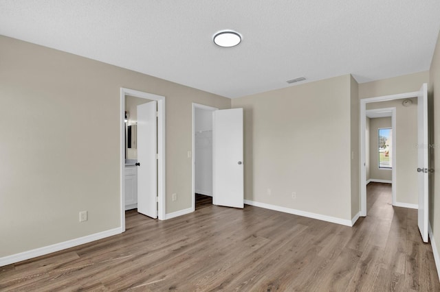 unfurnished bedroom featuring a closet, visible vents, ensuite bathroom, wood finished floors, and baseboards