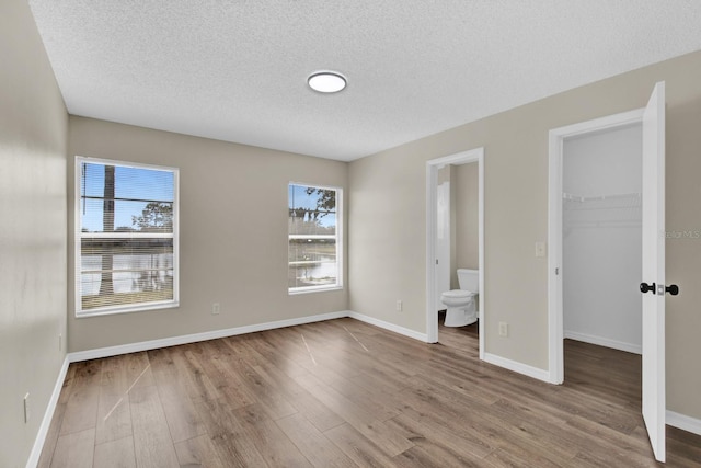 unfurnished bedroom with baseboards, wood finished floors, a spacious closet, a textured ceiling, and a closet