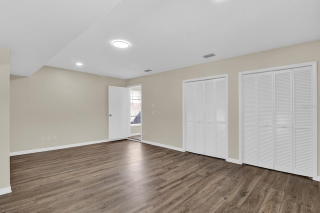 unfurnished bedroom featuring wood finished floors, baseboards, and two closets