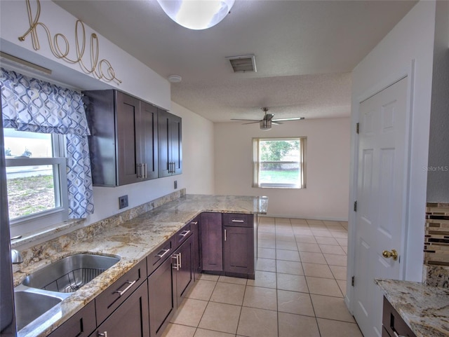 kitchen with kitchen peninsula, sink, light tile patterned floors, ceiling fan, and light stone counters