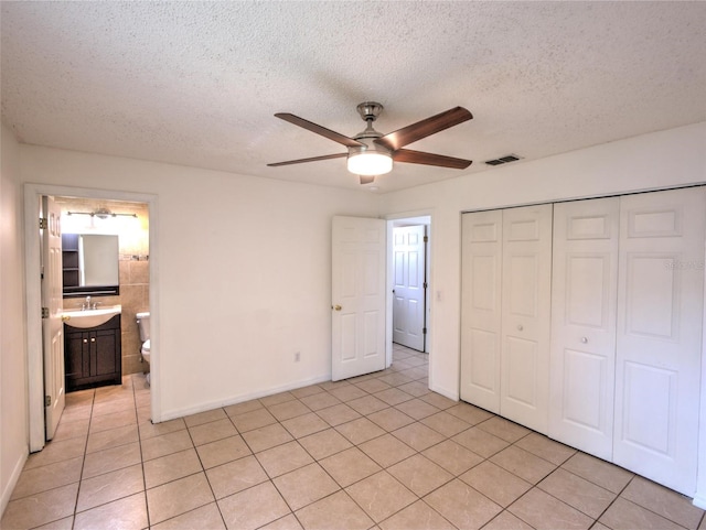 unfurnished bedroom featuring sink, light tile patterned floors, ceiling fan, a textured ceiling, and a closet