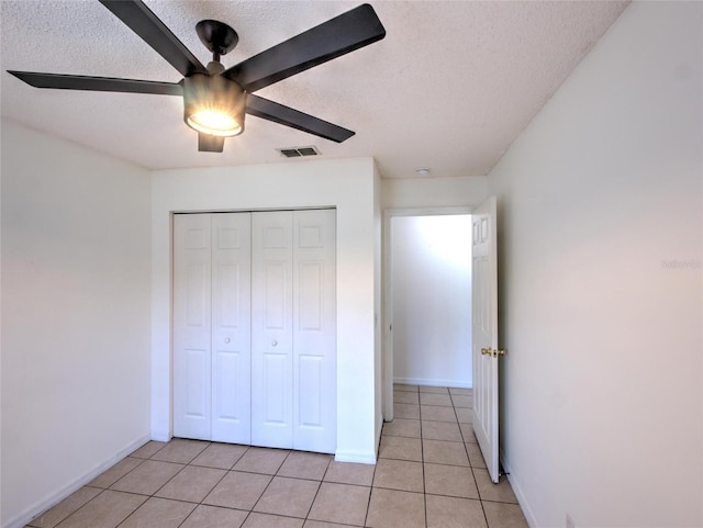 unfurnished bedroom with light tile patterned floors, a closet, a textured ceiling, and ceiling fan