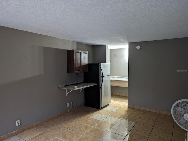 kitchen featuring stainless steel fridge, kitchen peninsula, a textured ceiling, and light tile patterned flooring