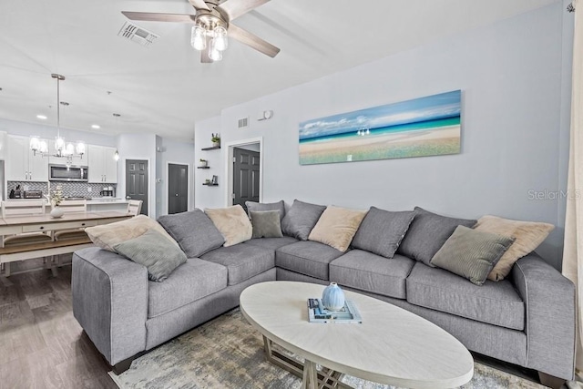 living room with ceiling fan with notable chandelier and dark wood-type flooring