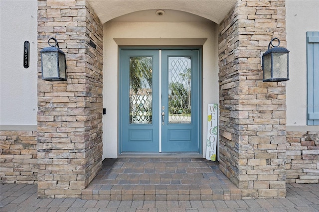 entrance to property featuring a shingled roof, stone siding, and french doors