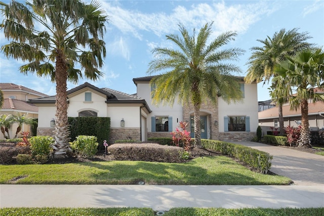 mediterranean / spanish-style house with decorative driveway, stone siding, and stucco siding