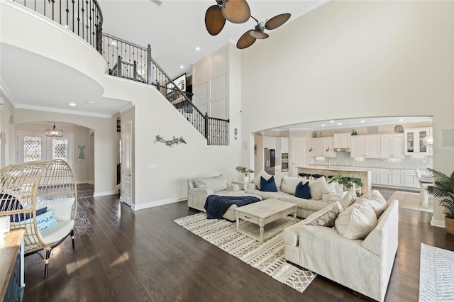 living area featuring baseboards, arched walkways, ornamental molding, dark wood-type flooring, and stairs