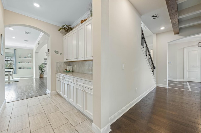 corridor featuring arched walkways, visible vents, crown molding, and light wood finished floors