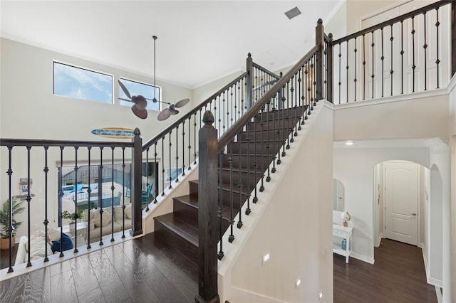 staircase with crown molding, a high ceiling, arched walkways, and wood finished floors