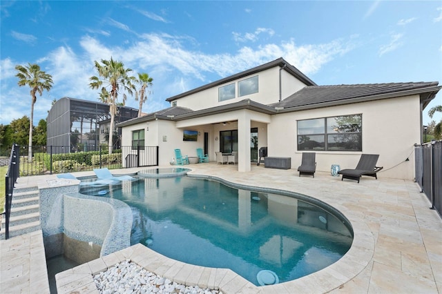 back of house with stucco siding, a pool with connected hot tub, fence, and a patio