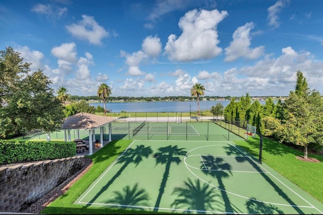 view of tennis court with a water view, community basketball court, fence, and a yard