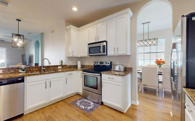 kitchen featuring appliances with stainless steel finishes, pendant lighting, white cabinetry, sink, and dark stone countertops