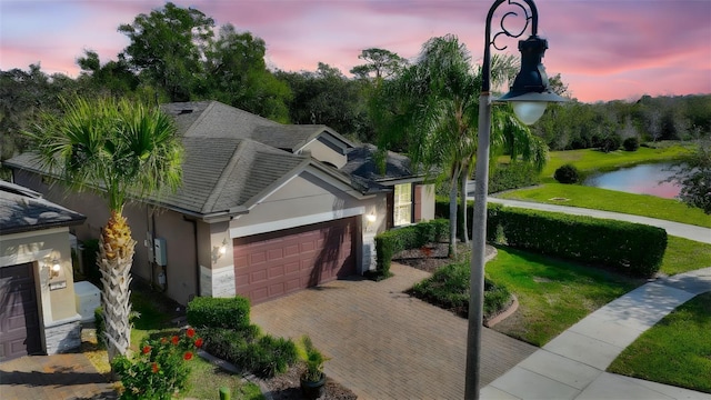 single story home with a garage, a water view, and a lawn