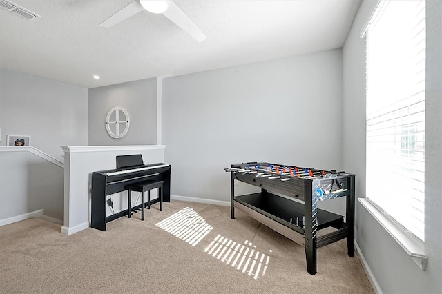 recreation room with a textured ceiling, light colored carpet, and ceiling fan