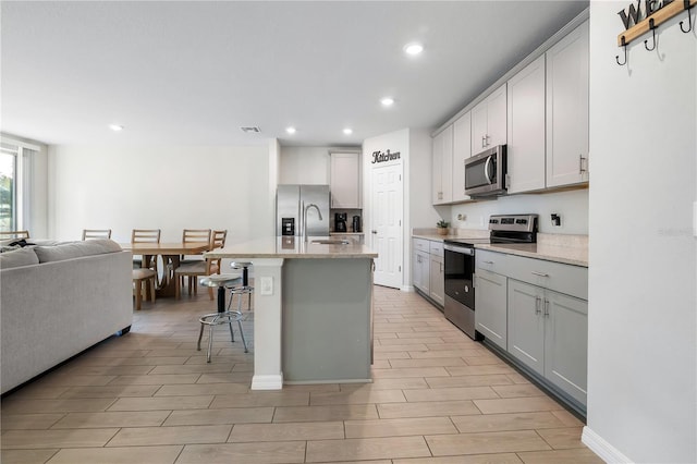 kitchen with sink, a kitchen breakfast bar, stainless steel appliances, light stone countertops, and a kitchen island with sink