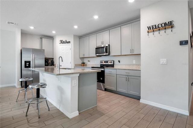 kitchen with a kitchen bar, sink, gray cabinets, an island with sink, and stainless steel appliances