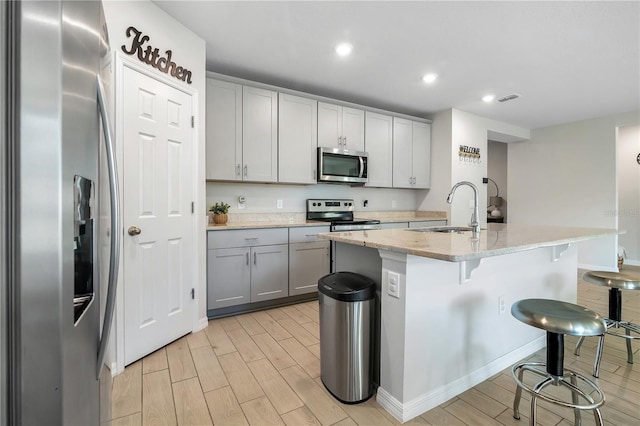 kitchen featuring sink, light stone counters, a center island with sink, appliances with stainless steel finishes, and gray cabinets