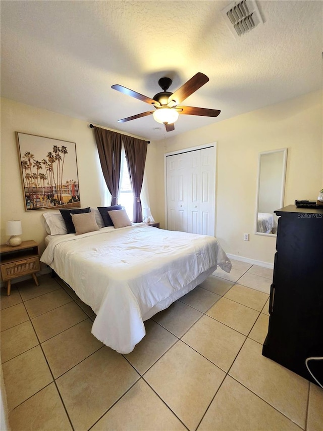 bedroom with ceiling fan, light tile patterned floors, a textured ceiling, and a closet