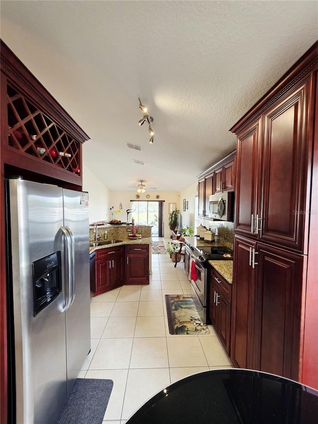 kitchen featuring appliances with stainless steel finishes, sink, light tile patterned floors, light stone countertops, and a textured ceiling